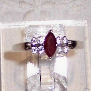 May include: A silver ring with a marquise-shaped ruby gemstone surrounded by smaller clear gemstones.