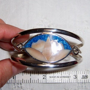 May include: Silver bangle bracelet with a blue and white inlay of a flower design. The bracelet is 2 inches wide.