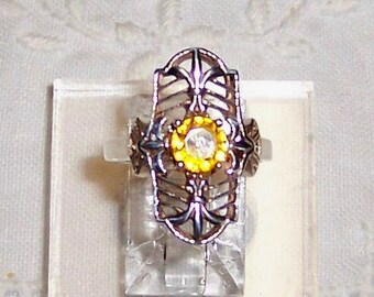 May include: A silver ring with a filigree design and a yellow and clear stone in the center.