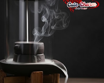 May include: A dark brown incense burner with a glass enclosure, wooden base, and a small black cup. White smoke rises from the burner, creating a visual effect. The text "Cute Charm corner" is in the upper right corner.