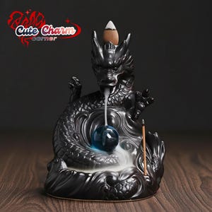 Puede incluir: Quemador de incienso de dragón de cerámica negra con un orbe azul y un incienso en forma de cono. El dragón tiene detalles intrincados y está colocado sobre una superficie de madera. El texto "Cute Charm corner" es visible.