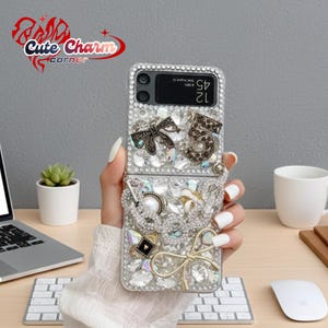 May include: A clear phone case encrusted with rhinestones and decorative embellishments. The case features a bow, the number 5, and other decorative elements. The phone displays the time as 12:45.
