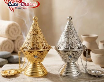 May include: Two ornate incense burners, one gold and one silver, with intricate filigree designs. Each burner has a conical lid, a chain, and a decorative base. The gold burner is on the left, and the silver burner is on the right. The text "Cute Charm Corner" is in the upper left corner.