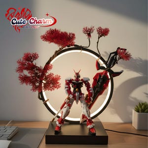 Puede incluir: Una figura de acción de robot rojo y blanco se encuentra sobre una base negra, enmarcada por una luz circular y ramas decorativas rojas. La lámpara tiene un marco negro y una luz blanca cálida. El diseño recuerda al arte japonés.