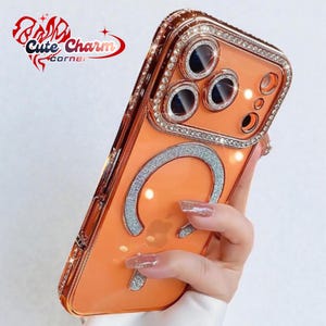 Puede incluir: Una funda de teléfono naranja con un acento plateado brillante y un anillo de pedrería alrededor de la cámara y los bordes. La funda tiene un diseño plateado brillante y está sujeta por una persona.