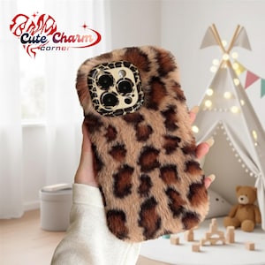 May include: A phone case with a brown and black leopard print design. The case has a furry texture and a camera lens cutout. The text "Cute Charm Corner" is visible in the upper left corner.