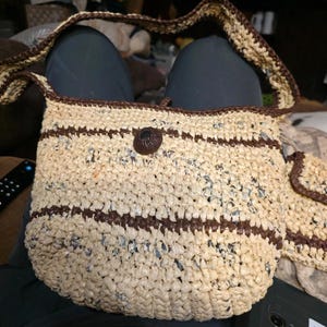 May include: A handmade crochet shoulder bag crafted from cream and dark brown plastic strips. The bag features a rectangular body with horizontal brown stripes, a matching brown shoulder strap, and a single dark brown circular button closure.