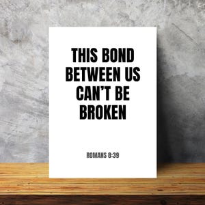 Può includere: Una stampa rettangolare bianca che presenta il testo nero THIS BOND BETWEEN US CAN'T BE BROKEN in un carattere sans-serif in grassetto, con il testo grigio più piccolo ROMANS 8:39 posizionato direttamente sotto il messaggio principale.