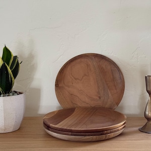 May include: A wooden serving tray and plates are stacked on a wooden surface. A potted snake plant with green and yellow leaves sits to the left. Two brass candle holders are on the right.