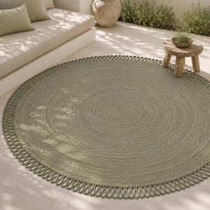 May include: A round sage green rug featuring a tightly woven centre and a decorative looped fringe border. The rug has a consistent circular pattern throughout the main body, with the outer edge finished in a series of uniform, elongated loops.