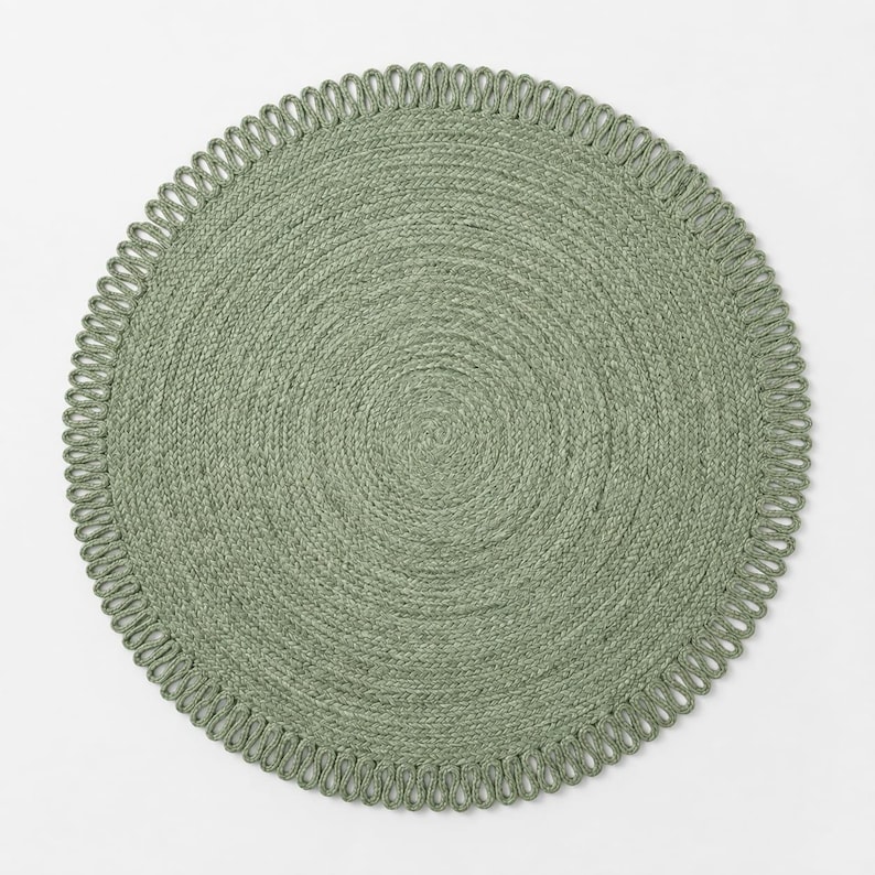 May include: A round sage green placemat featuring a tightly coiled braided centre and a decorative looped edge border. The placemat has a uniform circular shape and a textured surface created by the woven material, providing a consistent colour.