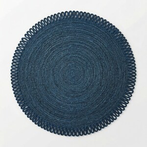 May include: A circular, deep navy blue rug featuring a tightly woven, concentric braided texture. The outer edge is finished with a decorative border of repeating, uniform loops that create a scalloped effect around the entire perimeter.