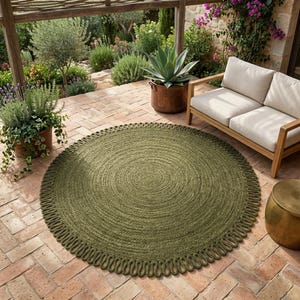 May include: A round, olive green area rug featuring a thick, braided texture and a decorative looped fringe border. The rug is constructed from natural fibres, showcasing a consistent circular weave pattern that radiates from the centre outwards.