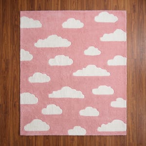 May include: A rectangular pink rug with a cloud pattern. The rug features white, fluffy cloud shapes scattered across the pink background. The rug is made of a soft, plush material, suitable for a child's room or nursery.
