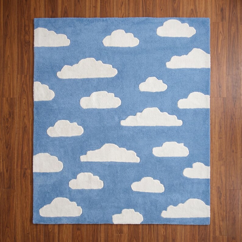 May include: A rectangular rug with a blue background and white cloud shapes scattered across it. The rug is made of a soft material and is designed to look like a sky with fluffy clouds. The rug is suitable for a child's room or a playful space.