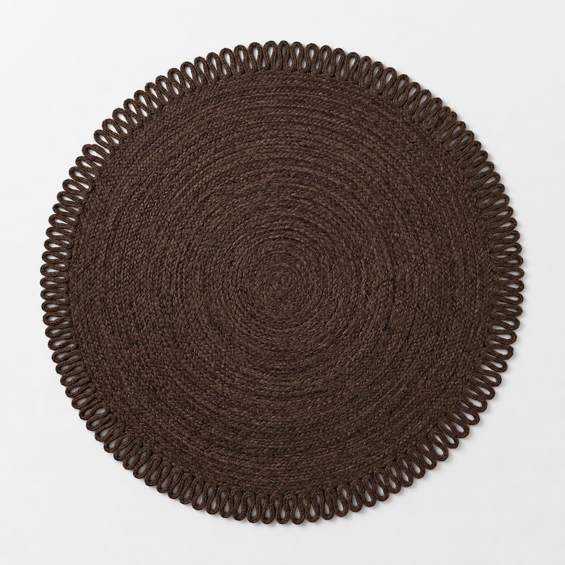 May include: A circular dark brown rug featuring a tightly woven centre and a decorative border composed of repeating, uniform loops. The rug has a consistent, textured appearance throughout, with the braided construction creating a radial pattern.