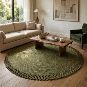 May include: A large, round, olive green area rug featuring a thick, braided texture and a decorative looped fringe border. The rug is crafted from natural fibres and sits flat on a wooden floor, providing a circular foundation for the living room.