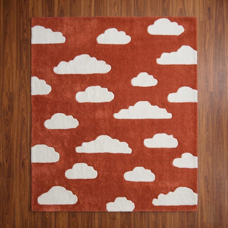 May include: A rectangular rug with a rust-colored background and white cloud shapes scattered across the surface. The rug has a soft, textured appearance, and the clouds are in various sizes and shapes.