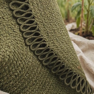 May include: An olive green textile item featuring a dense, woven knit construction. A prominent decorative trim runs along the edge, consisting of a continuous series of looped, braided cord detailing in a matching olive green shade.