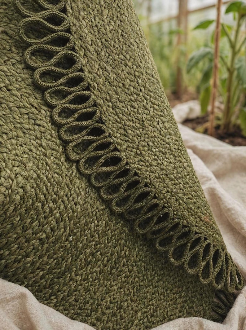 May include: An olive green textile item featuring a dense, woven knit construction. A prominent decorative trim runs along the edge, consisting of a continuous series of looped, braided cord detailing in a matching olive green shade.