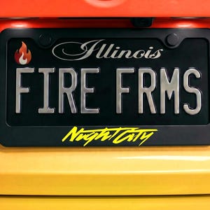 May include: Black license plate frame with the text "Illinois" and "FIRE FRMS" in silver lettering. A flame graphic is in the upper left corner. The words "Night City" are in yellow script at the bottom.