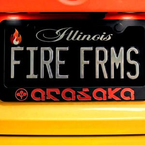 May include: Black license plate with the text "FIRE FRMS" in silver, and "Illinois" in silver script. A flame graphic is in the upper left corner. The word "arasaka" is in red at the bottom. The background is yellow and orange.