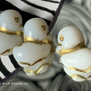 May include: Three white glass duck figurines with gold accents. The ducks are sitting on a black and white striped surface.