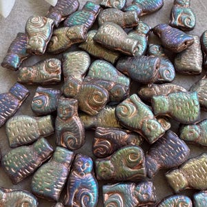 May include: A selection of iridescent glass beads shaped like fish and cats. The beads have a metallic finish with colours ranging from green and gold to blue and purple. These decorative beads are suitable for jewellery making and crafts.