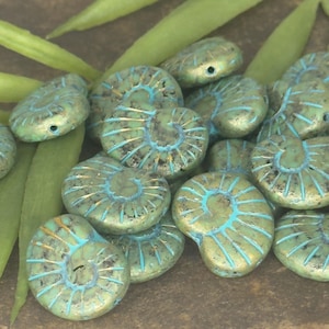 May include: A collection of teal-colored, spiral-shaped beads with turquoise and gold accents. The beads are arranged with green leaves in the background, creating a natural aesthetic. These beads are ideal for jewelry making.