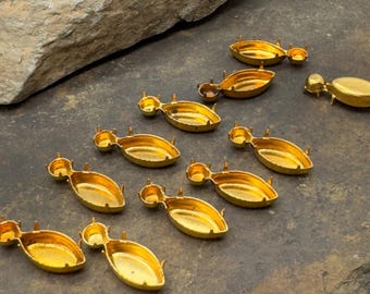 May include: A set of ten gold-toned metal settings for cabochons. The settings are oval shaped and have four prongs on each side.