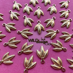 May include: A collection of 25 gold-toned metal leaf-shaped charms with a loop at the top. The charms are arranged in a circular pattern on a pink surface.