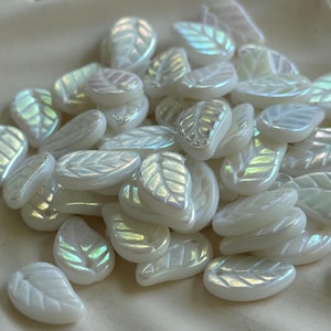 May include: A collection of iridescent white leaf-shaped beads. Each bead has a detailed leaf vein pattern and a pearlescent sheen, reflecting a spectrum of colors. These decorative beads are ideal for jewelry making and craft projects.
