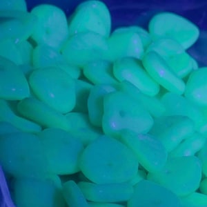 Puede incluir: Primer plano de un montón de piedras redondeadas y brillantes en tonos verdes y azules. Las piedras tienen un aspecto liso y pulido y están iluminadas, creando un efecto vibrante y luminoso. Ideal para decoración.