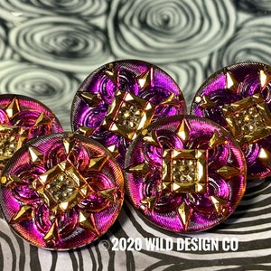 May include: Five iridescent purple and gold buttons with a starburst design. The buttons have a metallic sheen and a raised, geometric center. The background features a black and white zebra print and a swirled pattern.