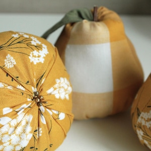 May include: Three decorative fabric pumpkins in a yellow and white floral pattern. The pumpkins are made of a soft, textured fabric and have a slightly rounded shape.