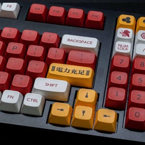 May include: A mechanical keyboard featuring a black base with a mix of red, white, and yellow keycaps. The yellow enter key displays the black text "電力充足". Other keys feature various symbols, numbers, and standard lettering.