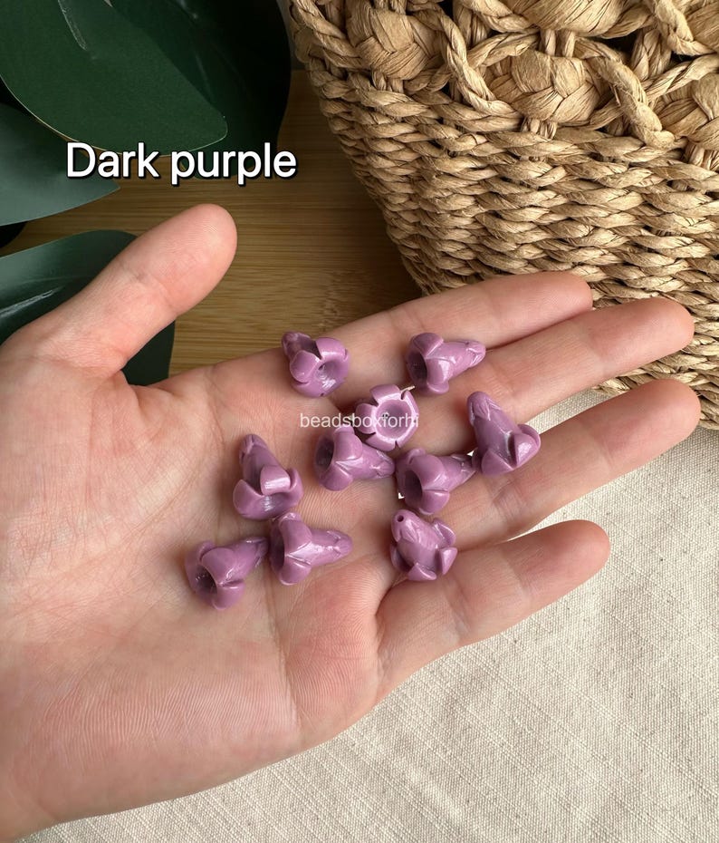 May include: A collection of small, dark purple beads shaped like flower buds with a smooth, glossy finish. Each bead features a central hole for threading. The text "Dark purple" and "beadsboxforhi" are visible in the image.