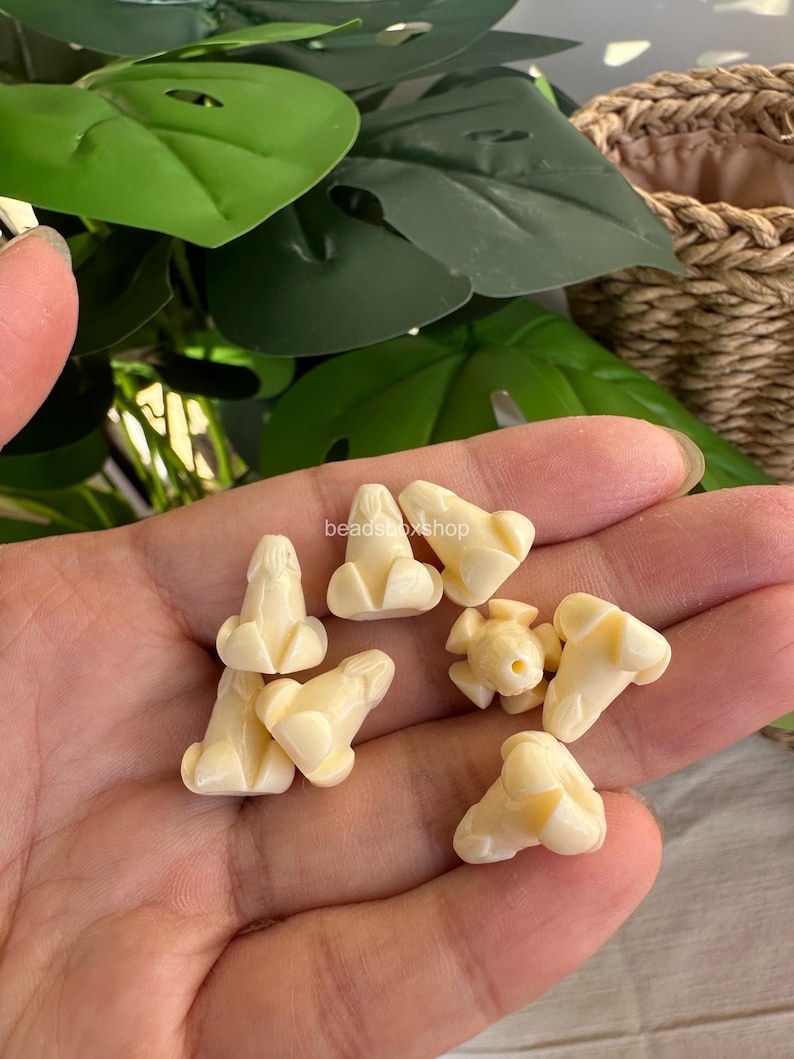 May include: A collection of small, off-white, phallic-shaped beads with a smooth, matte finish. Each bead features a distinct, carved structure with a rounded top and a flared base, designed for threading. The text beadsboxshop is visible.