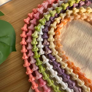 May include: Multiple strands of flower-shaped beads in various pastel colors including pink, green, white, purple, and orange. Each strand features a repeating floral design. The text beadsboxshop is visible on the strands.