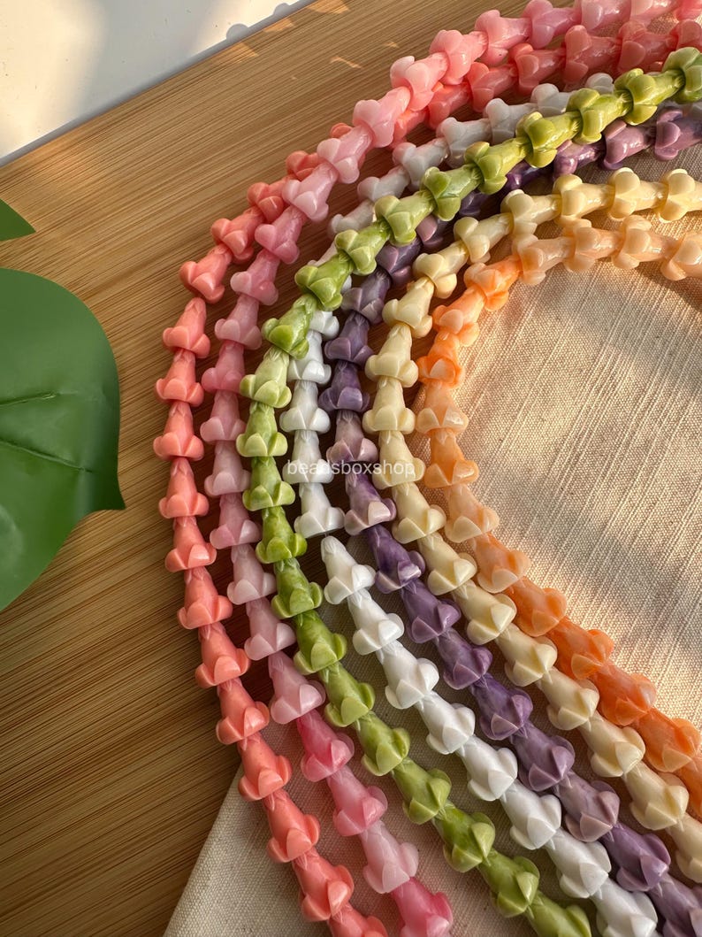 May include: Multiple strands of flower-shaped beads in various pastel colors including pink, green, white, purple, and orange. Each strand features a repeating floral design. The text beadsboxshop is visible on the strands.