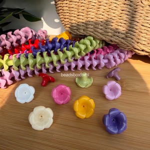 May include: A collection of colorful plastic beads and flower-shaped components. The beads are linked together in various colors, including pink, green, purple, and red. Several flower-shaped beads in white, pink, yellow, and purple are scattered on a wooden surface.