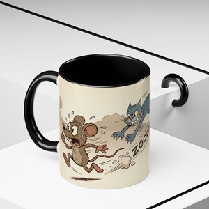 May include: A ceramic mug with a black handle and interior. The exterior features a cartoon illustration of a mouse running from a blue cat, with the word "ZOOM" in the background. The mug has a beige background.
