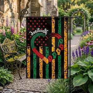 May include: A black garden flag with a design celebrating Juneteenth. The flag features a heart-shaped design with red, yellow, and green stripes, and raised fists. The words "Juneteenth" are written in white script. The background has a distressed look.