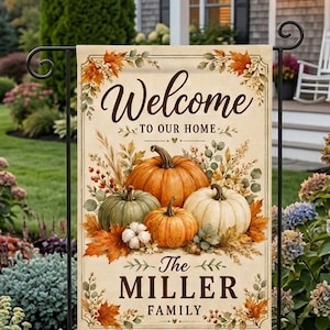 May include: A rectangular garden flag featuring a cream background with a decorative border of autumn leaves. The text reads Welcome TO OUR HOME and The MILLER FAMILY. A central illustration displays orange, green, and white pumpkins.