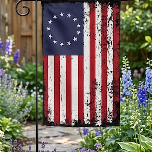 May include: A rectangular garden flag featuring a distressed Betsy Ross American flag design with thirteen white stars arranged in a circle on a blue field, accompanied by alternating red and white vertical stripes with black weathered edges.