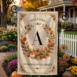 May include: A rectangular garden flag featuring a cream-colored background with vertical stripes. The design includes a central letter A surrounded by a wreath of autumn leaves and pumpkins. The text reads WELCOME and ANDERSON'S FAMILY.
