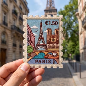 May include: A rectangular embroidered patch shaped like a postage stamp featuring a scene of Paris. The design includes the Eiffel Tower, Notre Dame, a river, a croissant, a cup of coffee, and the text €1.50 and PARIS in dark brown thread.