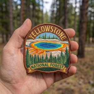 May include: An embroidered patch featuring a landscape of Yellowstone National Forest. The design includes a central blue thermal pool surrounded by orange and yellow rings, set against a backdrop of green pine trees and the text Yellowstone National Forest.