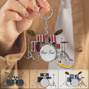 May include: Miniature red drum set keychain with silver hardware. The drum set has a white drum with the text "Your Text". The keychain is held by a hand. Additional drum set images are shown below.