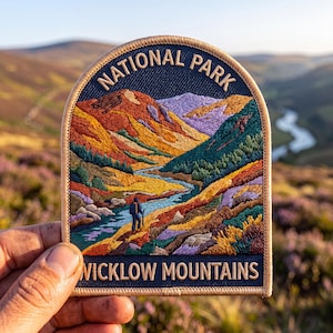 May include: An embroidered patch with a beige border featuring a landscape of the Wicklow Mountains. The design includes a hiker, a winding blue river, and colorful hills in shades of orange, yellow, purple, and green. Text reads NATIONAL PARK.